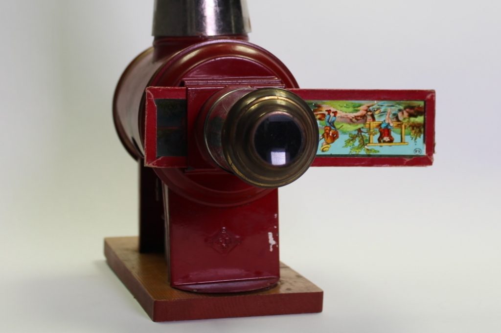Frontansicht eines roten Projektionsapparates nach Art einer Laterna Magica mit eingelegtem Glasbild.